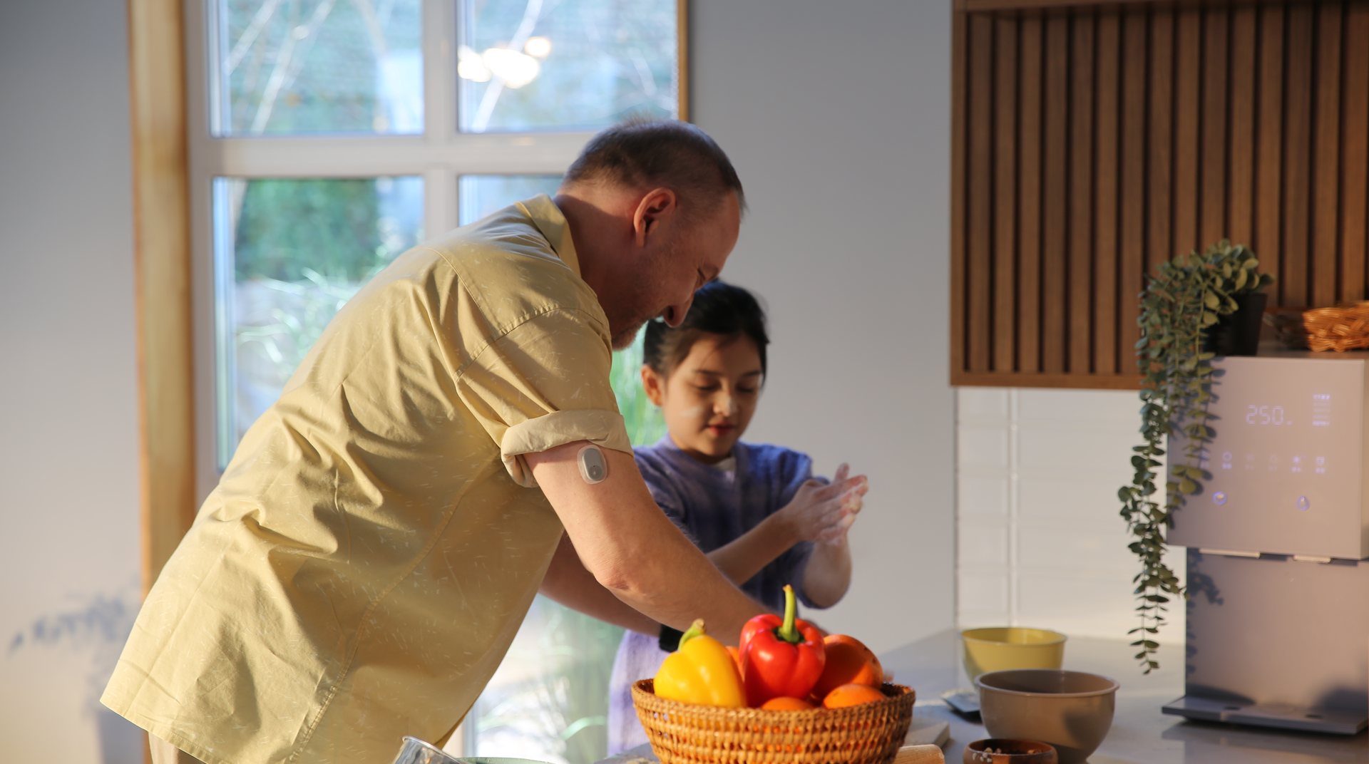 A man wearing a CareSens Air sensor on his upper arm, baking at a kitchen counter with his daughter.