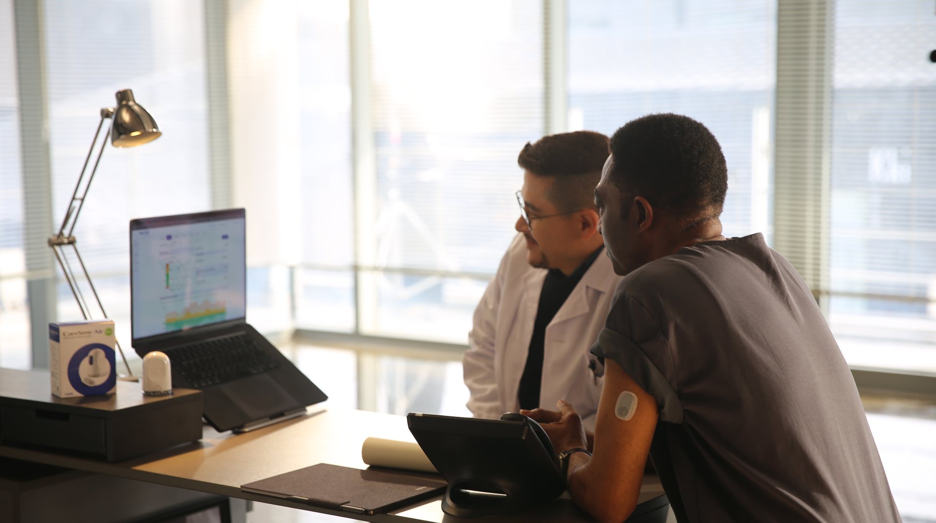 A clinician and a person wearing a CareSens Air sensor reviewing glucose data together.